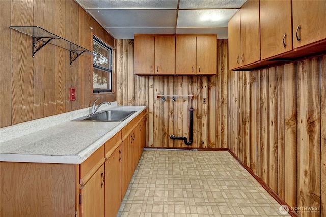 kitchen featuring wooden walls, light floors, light countertops, brown cabinetry, and a sink