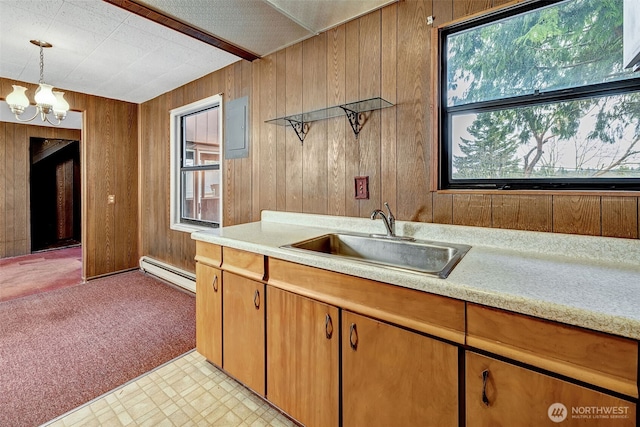 kitchen with a sink, a baseboard heating unit, an inviting chandelier, wood walls, and light countertops