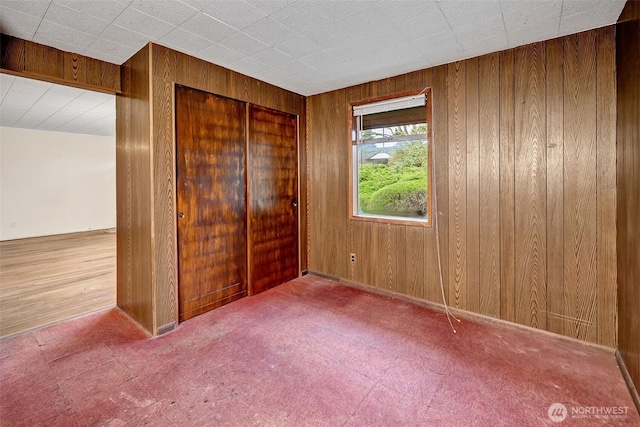 unfurnished bedroom featuring carpet flooring, a closet, and wood walls