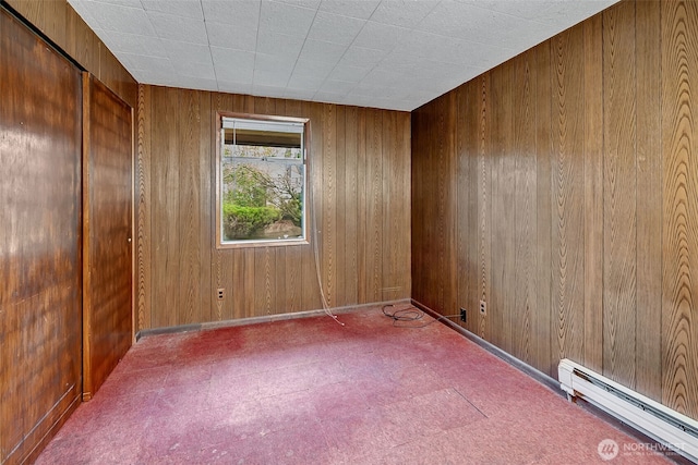 unfurnished room with a baseboard heating unit and wood walls