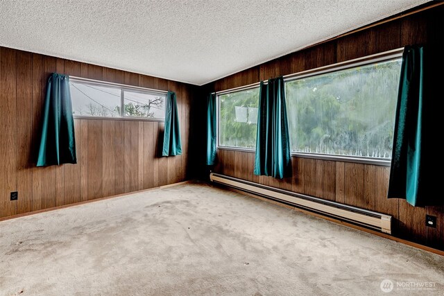 empty room featuring a textured ceiling, carpet, wood walls, and a baseboard radiator