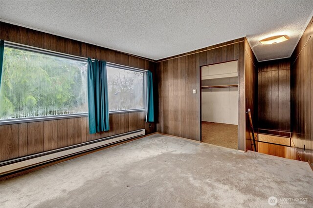 unfurnished bedroom with wooden walls, multiple windows, baseboard heating, and carpet floors