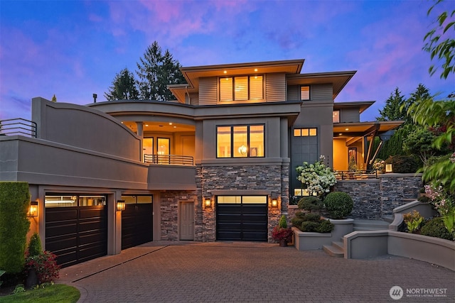 view of front facade with stucco siding, decorative driveway, stone siding, a garage, and a balcony