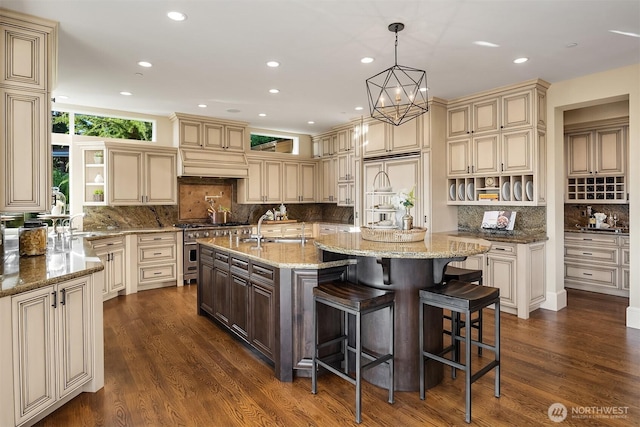 kitchen featuring dark wood finished floors, a center island with sink, high quality appliances, cream cabinetry, and open shelves