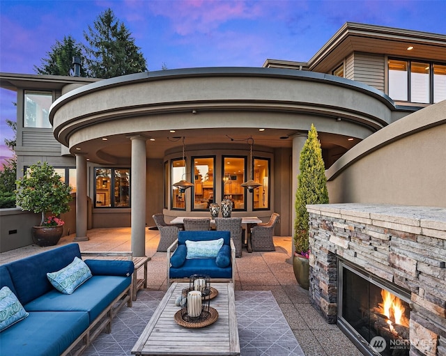 patio terrace at dusk with outdoor dining space and an outdoor living space with a fireplace