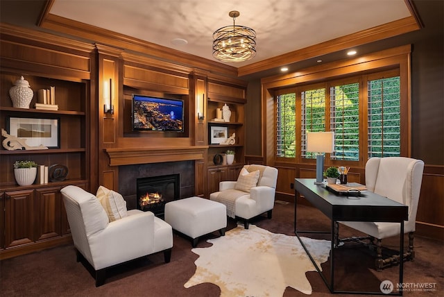 living area featuring built in features, crown molding, an inviting chandelier, and a glass covered fireplace