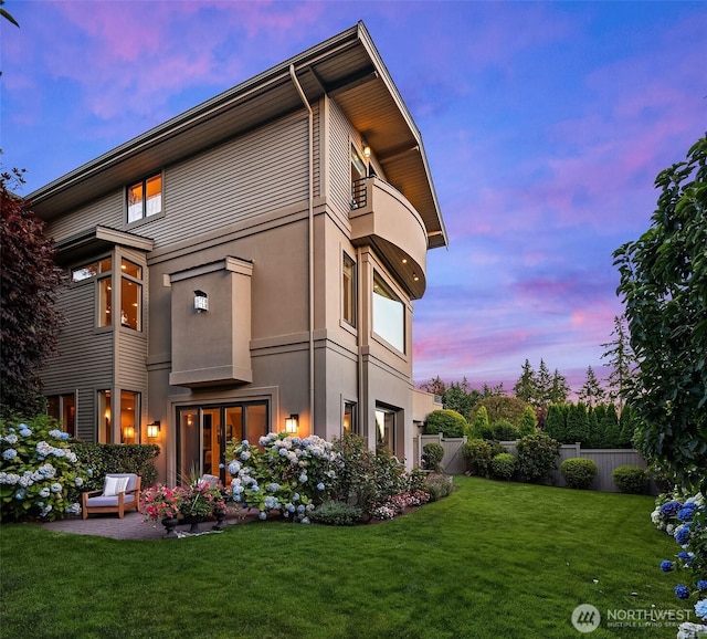 back of property at dusk featuring a patio, fence, a lawn, and stucco siding