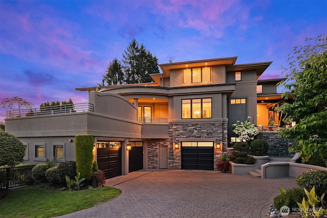 view of front of home featuring a balcony, an attached garage, stucco siding, stone siding, and decorative driveway