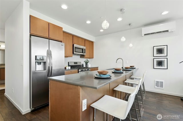 kitchen featuring visible vents, appliances with stainless steel finishes, brown cabinetry, a wall mounted air conditioner, and a kitchen bar