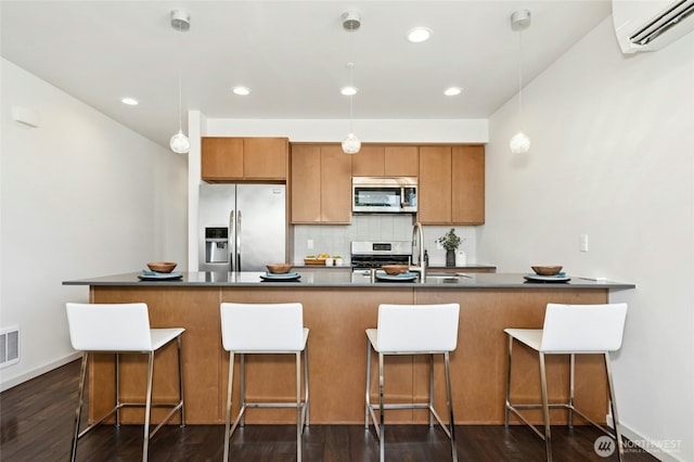 kitchen featuring tasteful backsplash, a wall unit AC, appliances with stainless steel finishes, brown cabinets, and a sink