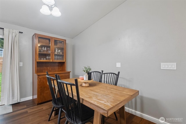 dining space featuring a chandelier, lofted ceiling, dark wood-style flooring, and baseboards