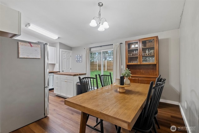 dining room featuring dark wood-type flooring, lofted ceiling, baseboards, and an inviting chandelier