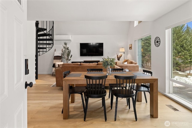 dining room featuring light wood-type flooring, stairway, a wall unit AC, and visible vents