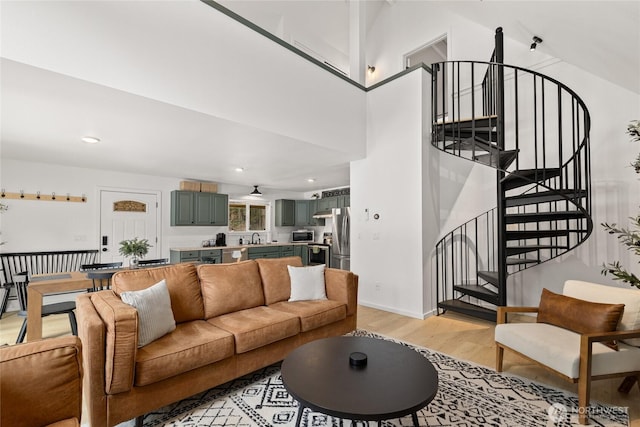 living room featuring light wood-style flooring, recessed lighting, a towering ceiling, baseboards, and stairs