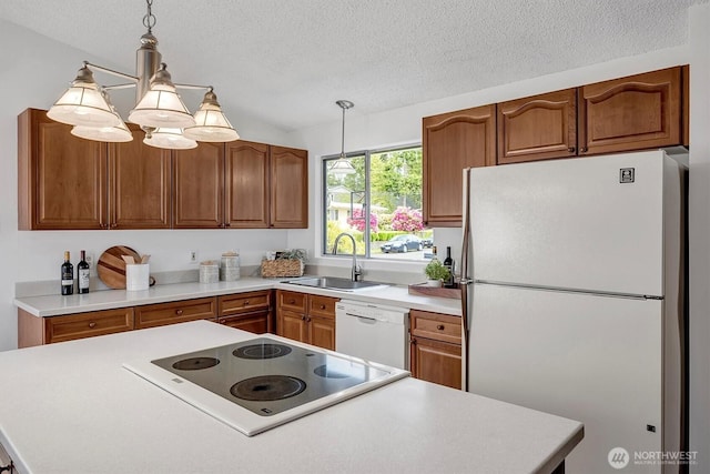 kitchen with white appliances, a sink, brown cabinets, a textured ceiling, and pendant lighting