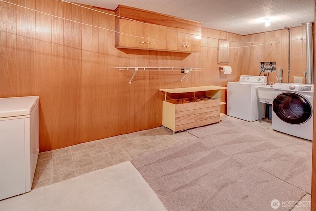 washroom featuring washer and clothes dryer, cabinet space, and wood walls