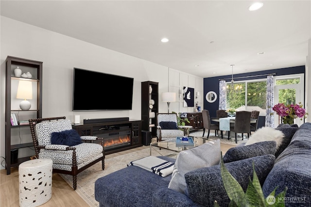 living room featuring a notable chandelier, a glass covered fireplace, recessed lighting, and light wood-style floors