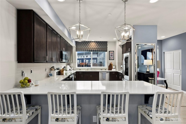 kitchen with a peninsula, stainless steel appliances, dark brown cabinetry, light countertops, and a chandelier