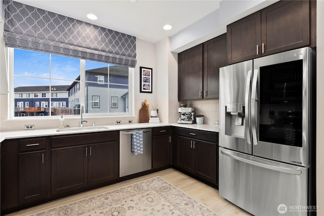 kitchen with dark brown cabinetry, light countertops, light wood-style floors, stainless steel appliances, and a sink