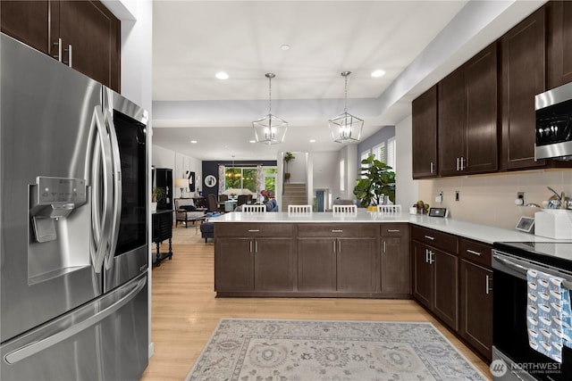 kitchen featuring light wood finished floors, open floor plan, light countertops, appliances with stainless steel finishes, and a peninsula