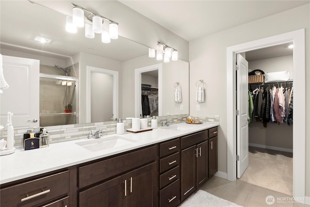 bathroom with vanity, baseboards, a stall shower, a walk in closet, and backsplash