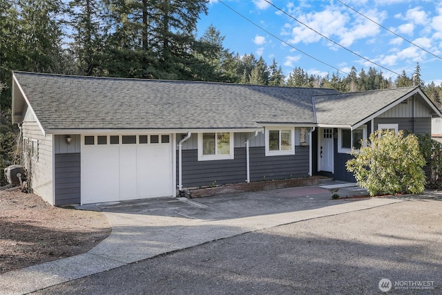 single story home with a garage, a shingled roof, and aphalt driveway