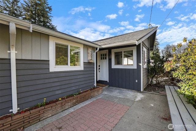 view of exterior entry featuring a patio area and roof with shingles