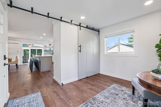 sitting room with a healthy amount of sunlight, wood finished floors, a wall unit AC, and a barn door