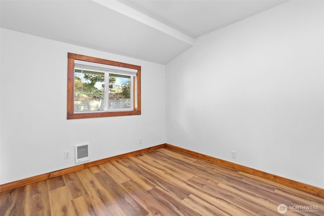 empty room with vaulted ceiling, wood finished floors, visible vents, and baseboards