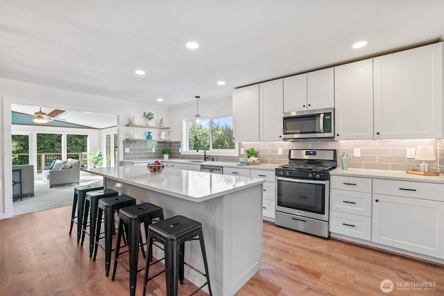 kitchen with stainless steel appliances, white cabinetry, a kitchen breakfast bar, and open shelves