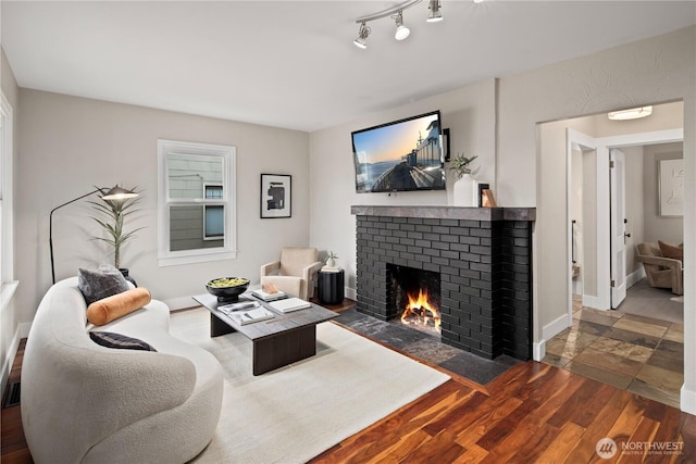 living area featuring track lighting, a fireplace, baseboards, and wood finished floors