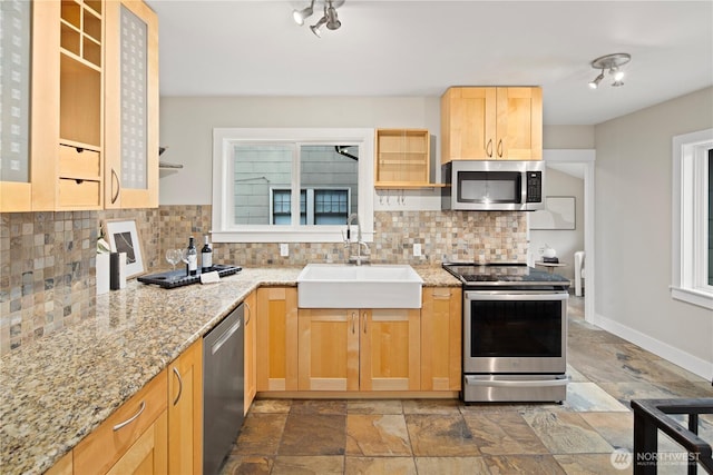 kitchen with baseboards, a sink, stainless steel appliances, light brown cabinetry, and backsplash