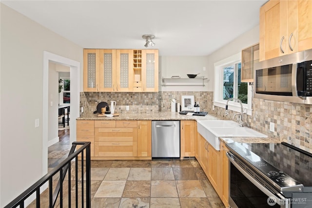 kitchen featuring tasteful backsplash, stone finish floor, appliances with stainless steel finishes, light brown cabinets, and a sink