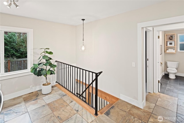 hallway featuring a wealth of natural light, stone finish floor, an upstairs landing, and baseboards