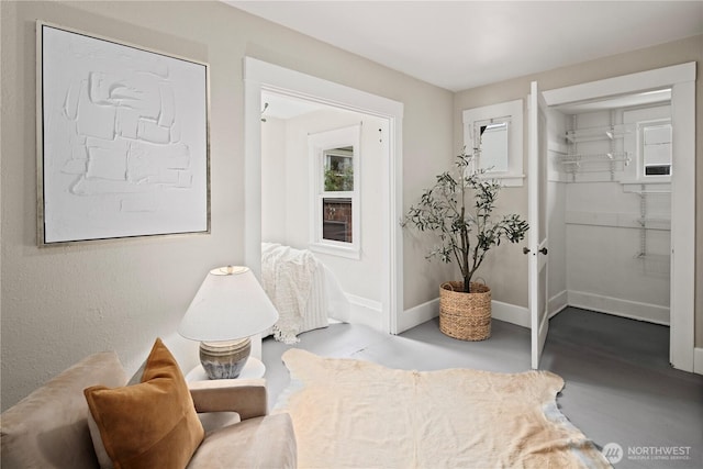 bedroom with a walk in closet, finished concrete floors, and baseboards