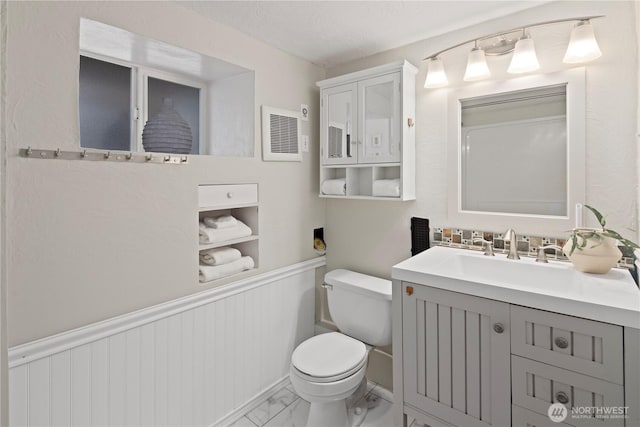 half bathroom with visible vents, toilet, a wainscoted wall, marble finish floor, and vanity