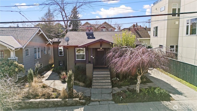 view of front of property with a shingled roof, a chimney, and fence