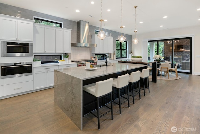 10906 SE 28th St, Bellevue, WA 98004 - kitchen with light wood-style flooring, a kitchen breakfast bar, wall chimney exhaust hood, an island with sink, and backsplash