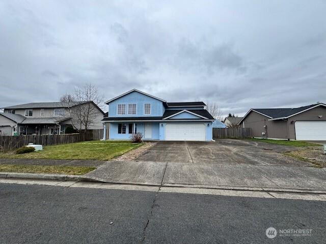 traditional home with concrete driveway, a front lawn, an attached garage, and fence