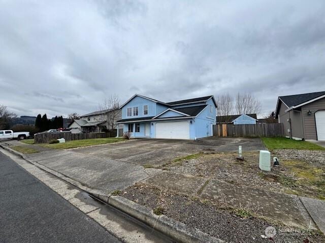 view of front facade featuring a garage, a residential view, concrete driveway, and fence