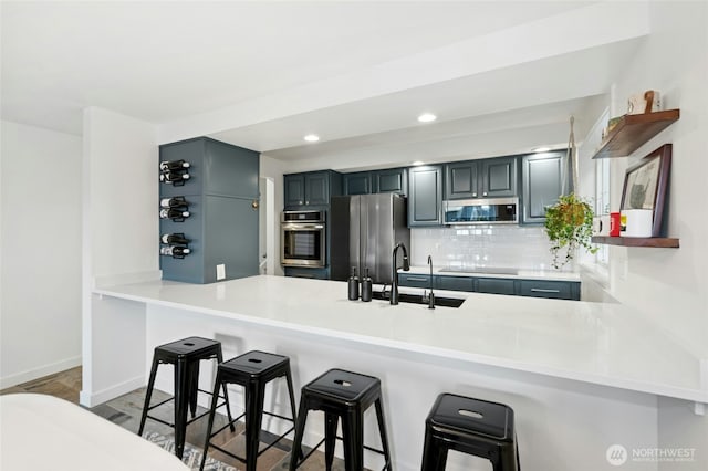 kitchen featuring a kitchen bar, decorative backsplash, appliances with stainless steel finishes, a peninsula, and a sink