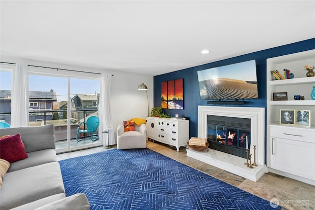 living area featuring a glass covered fireplace, built in features, and recessed lighting