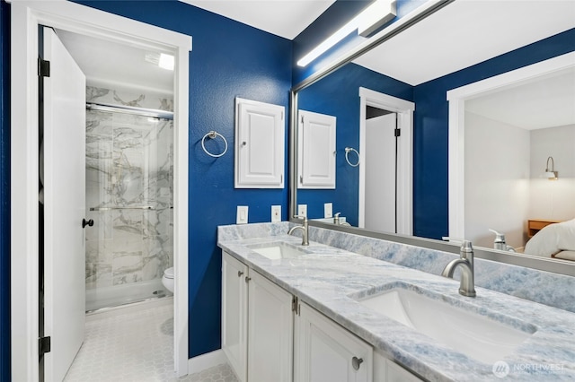 full bathroom featuring double vanity, toilet, a marble finish shower, and a sink