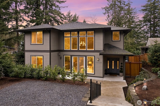 back of property at dusk with a shingled roof, a gate, and fence