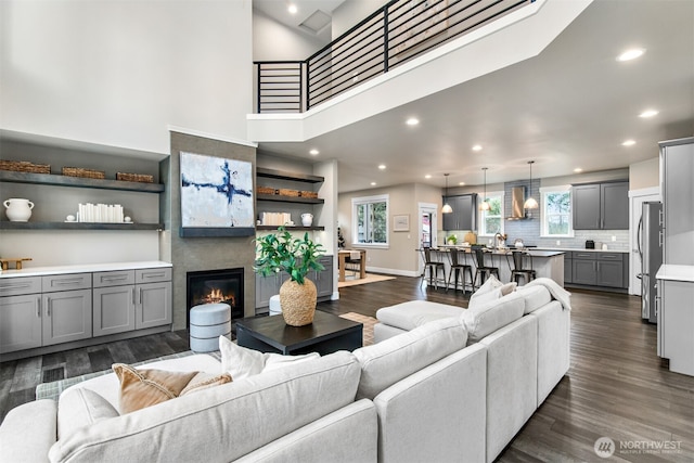 living area with baseboards, a glass covered fireplace, dark wood-style flooring, a high ceiling, and recessed lighting