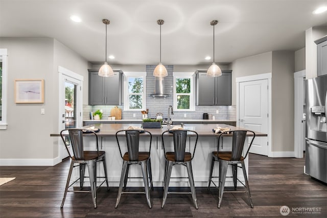 kitchen featuring wall chimney exhaust hood, backsplash, stainless steel fridge, and a kitchen breakfast bar