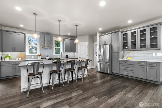 kitchen featuring gray cabinetry, a breakfast bar, wall chimney range hood, stainless steel fridge, and dark wood finished floors