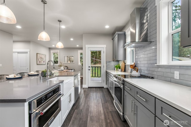 kitchen with dark wood finished floors, wall chimney exhaust hood, gray cabinets, stainless steel appliances, and backsplash