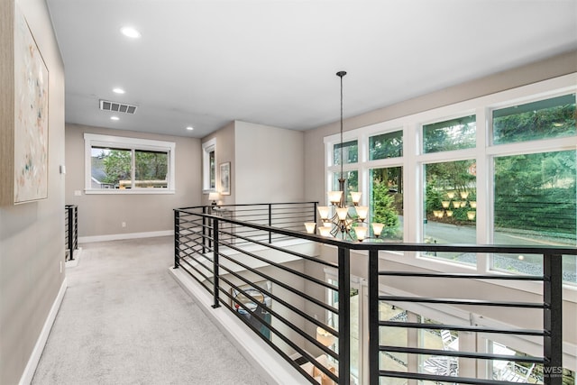 hallway featuring baseboards, visible vents, an inviting chandelier, an upstairs landing, and carpet floors