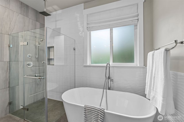 bathroom with a stall shower, a freestanding tub, and tile walls